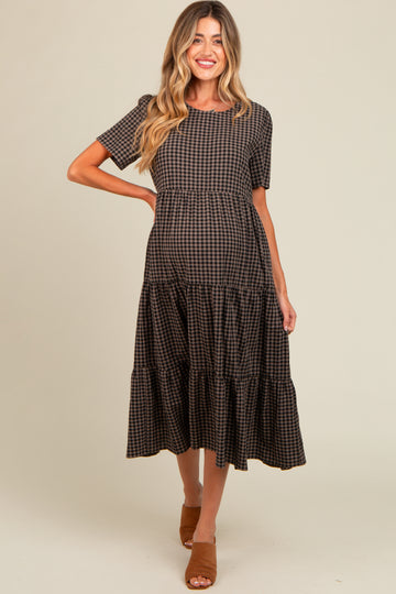 woman wearing a brown and black checked maternity dress with tiered skirts and short sleeves, showing her baby bump