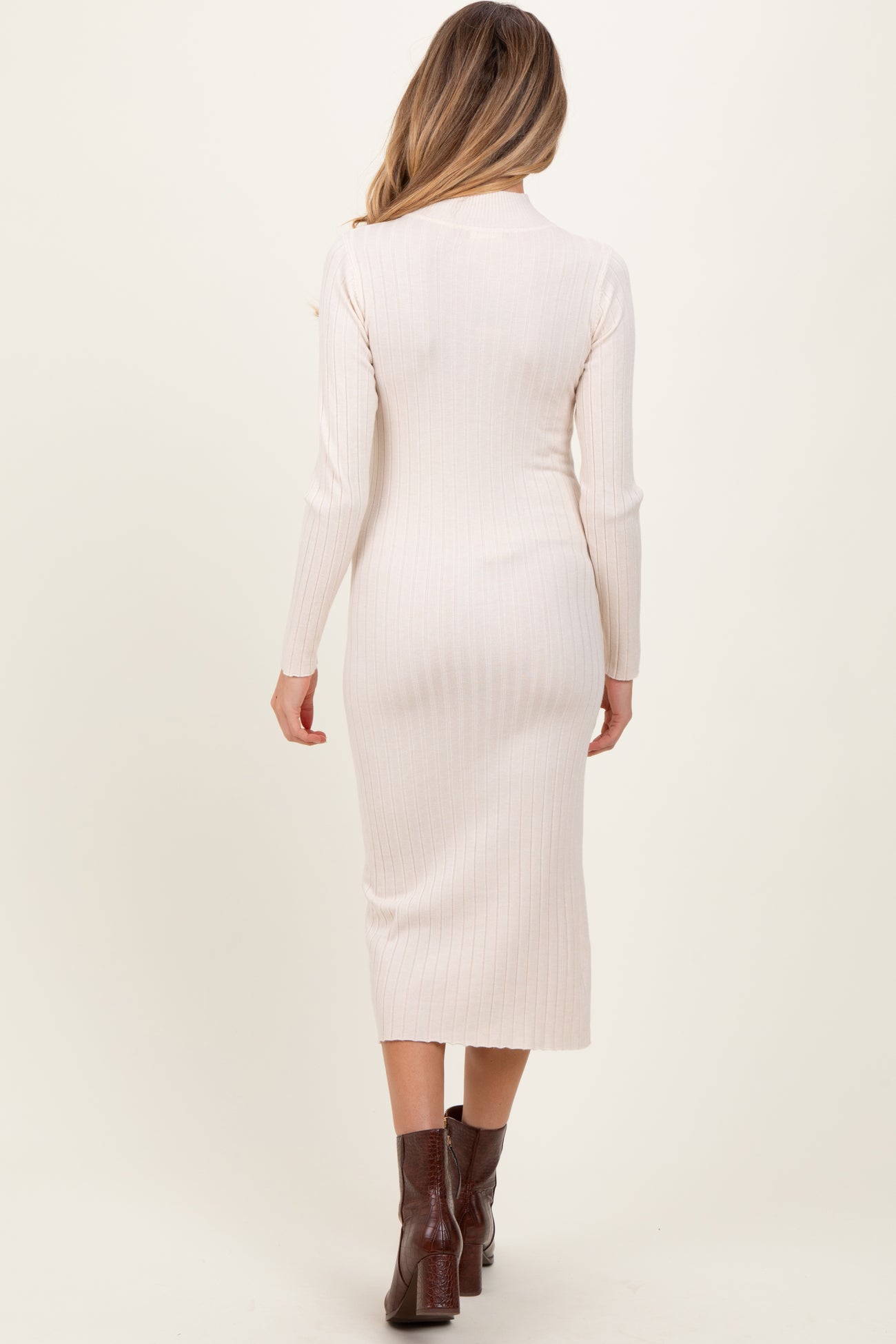 woman wearing a cream ribbed long sleeve maternity dress with a fitted silhouette and a midi length