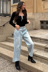 woman wearing a black long sleeve top with tie detail and light wash wide-leg jeans, standing on outdoor steps