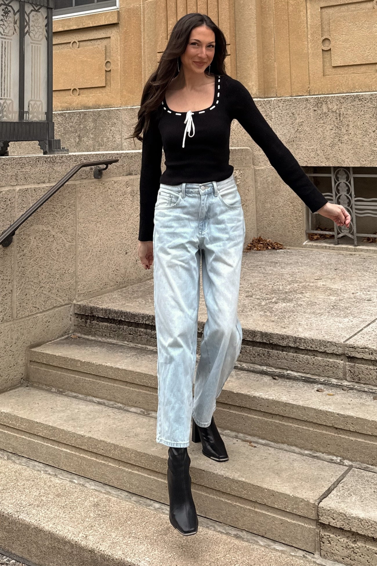 woman wearing a black ribbed long sleeve top with button details and light wash straight leg jeans with black ankle boots
