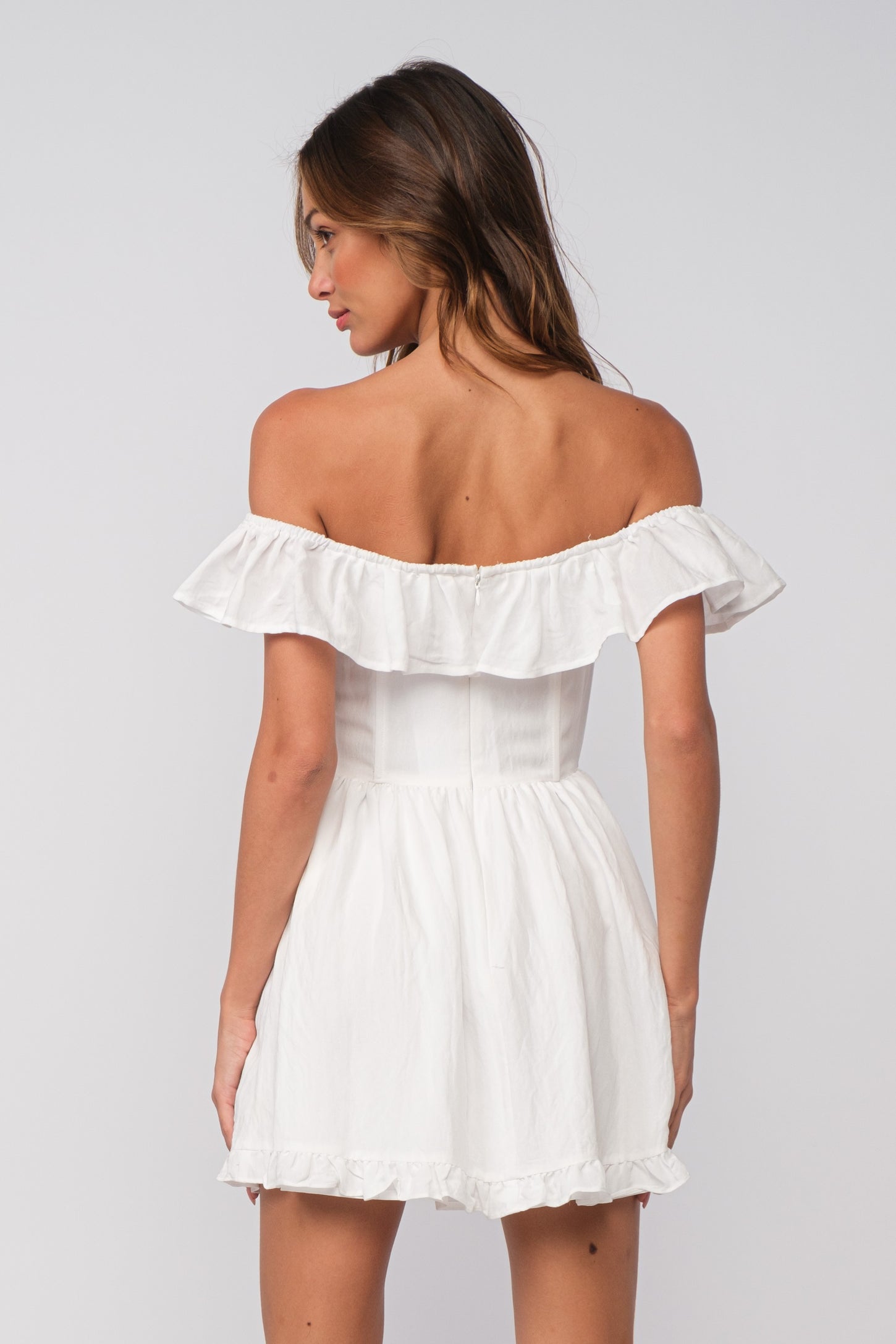 woman wearing a white off-the-shoulder dress with ruffled detail and a fitted bodice, shown from the back
