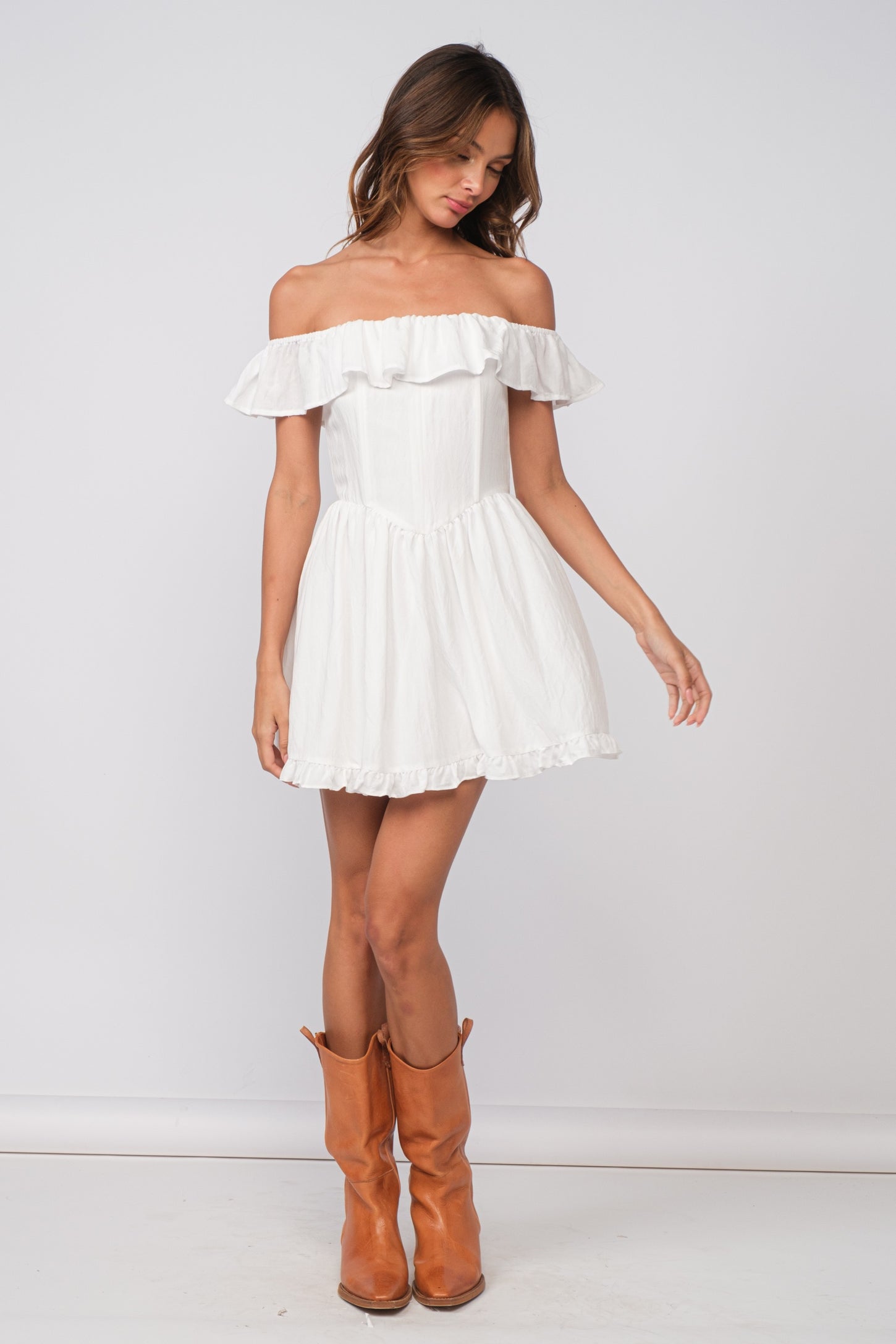 woman wearing a white off-the-shoulder mini dress with ruffled details and brown knee-high boots