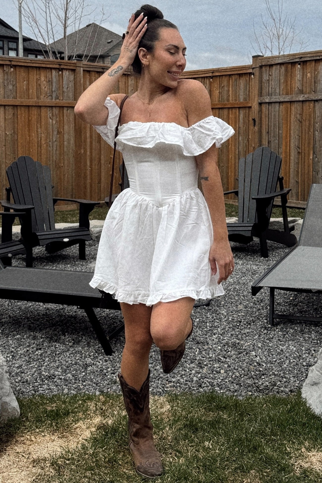 woman wearing a white off-the-shoulder mini dress with ruffle details and brown cowboy boots