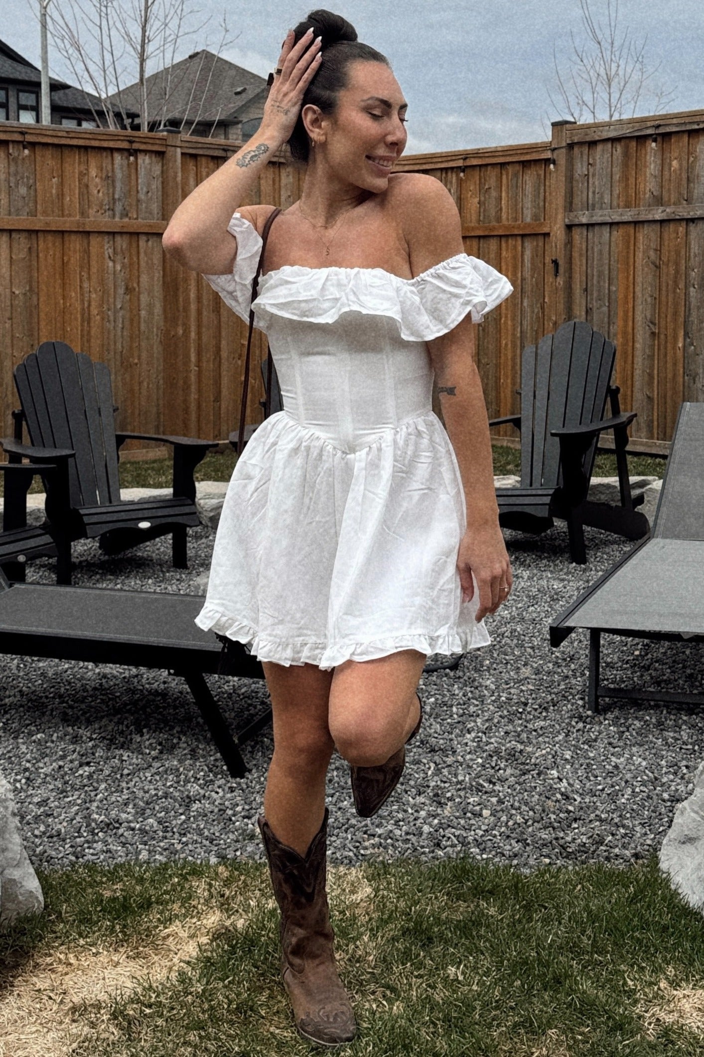 woman wearing a white off-the-shoulder mini dress with ruffle details and brown cowboy boots