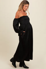 woman wearing a black off-the-shoulder maternity dress with long sleeves and a smocked bodice, showing her baby bump