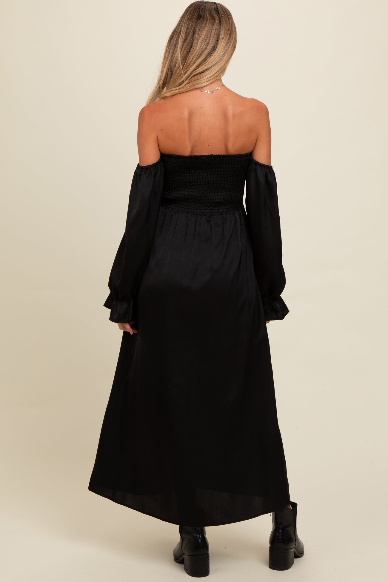 woman wearing a black off-the-shoulder maternity dress with long sleeves and a smocked bodice, showing a stylish back view