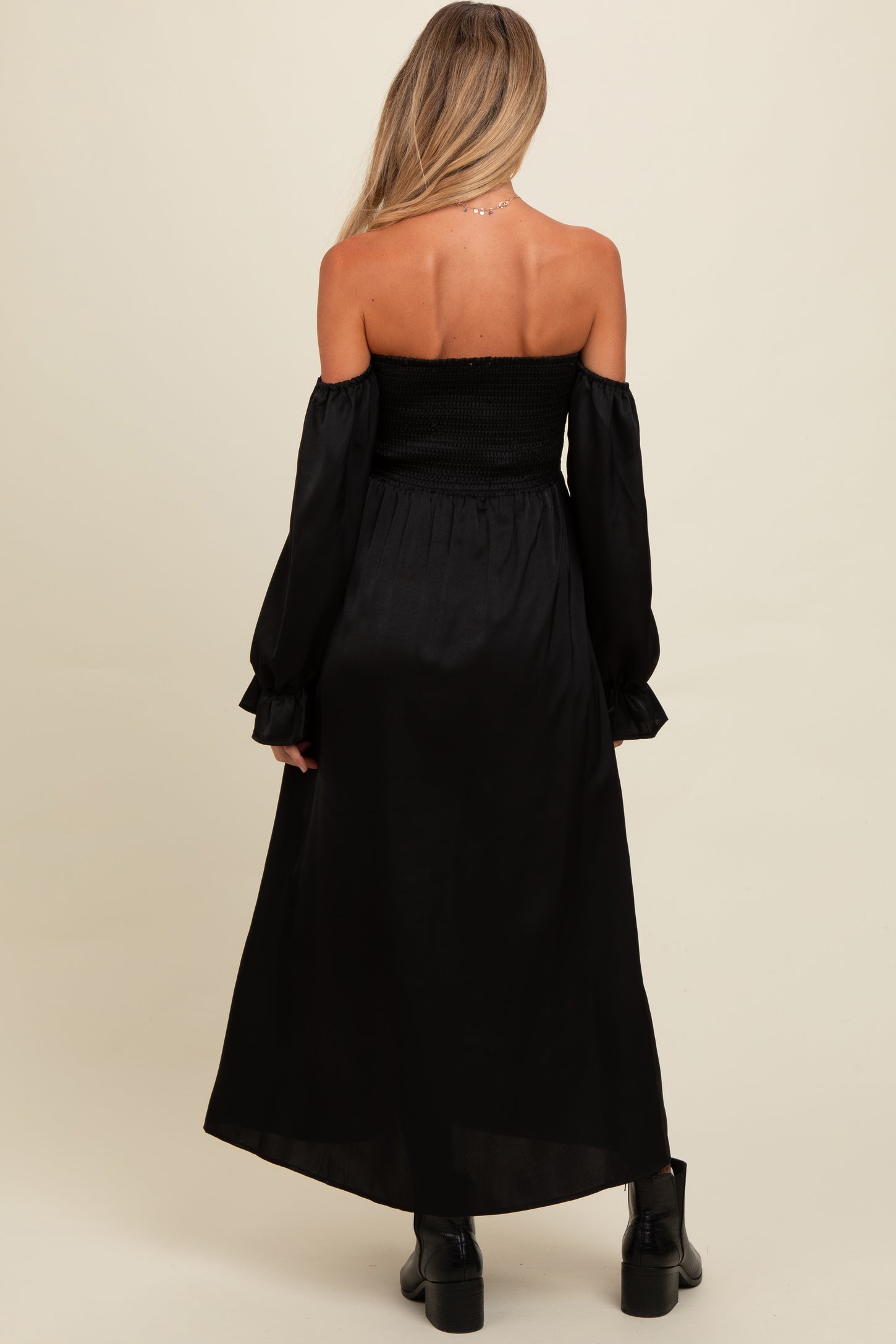 woman wearing a black off-the-shoulder maternity dress with long sleeves and a smocked bodice, showing a stylish back view