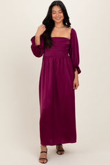 woman wearing a fuchsia long sleeve maxi dress with a ruched bodice and puff sleeves, standing and smiling