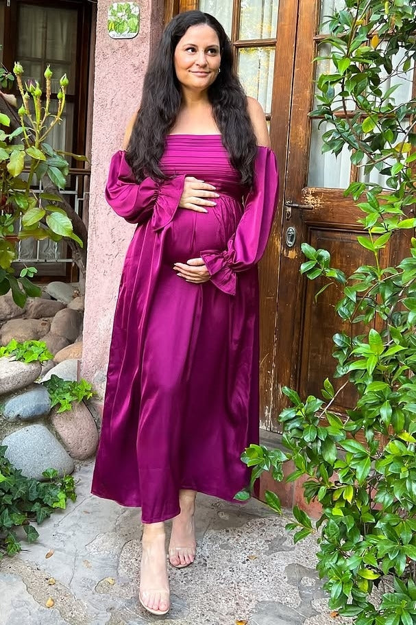 woman wearing a deep pink off-shoulder maternity dress with long sleeves and holding her baby bump