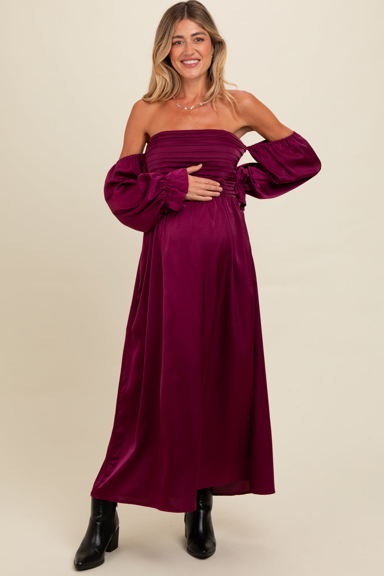 woman wearing a burgundy off-the-shoulder maternity gown with puffed sleeves and holding her baby bump