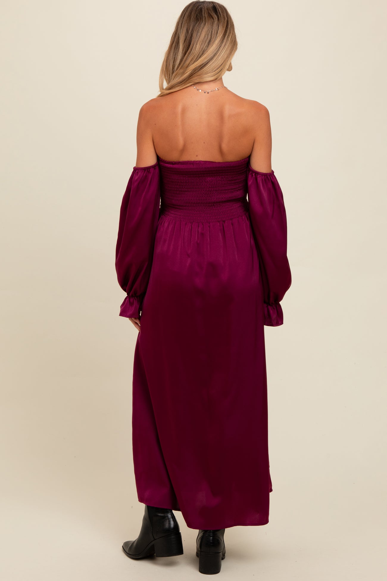 woman wearing a burgundy off-the-shoulder maternity maxi dress with long puff sleeves and a smocked bodice, showing her back