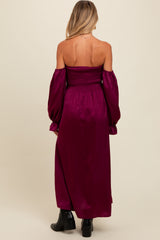 woman wearing a burgundy off-the-shoulder maternity maxi dress with long puff sleeves and a smocked bodice, showing her back