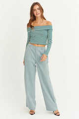 woman wearing a green and white striped off-the-shoulder crop top and light blue wide-leg pants