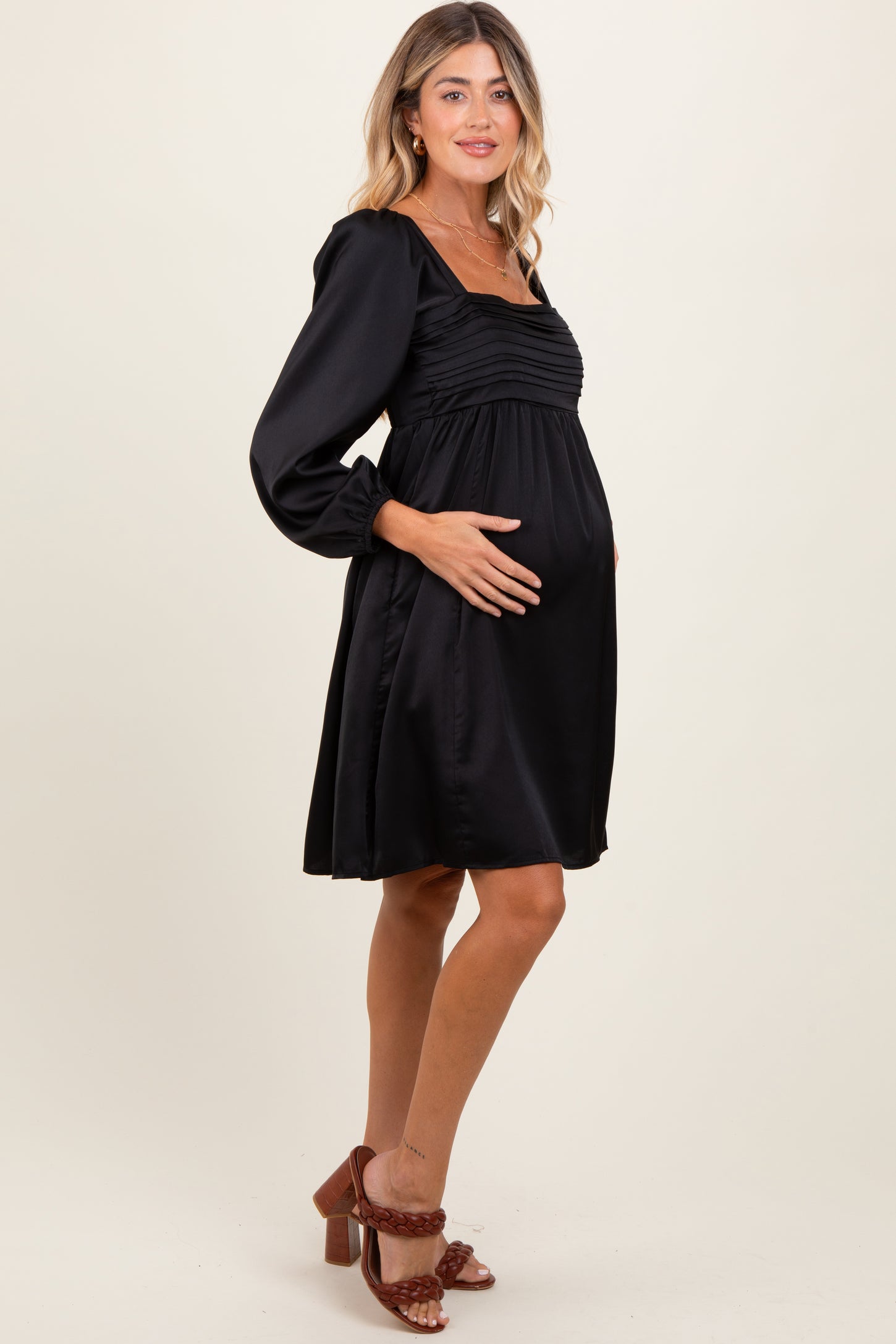 woman wearing a black maternity dress with ruched detailing and long sleeves, holding her baby bump