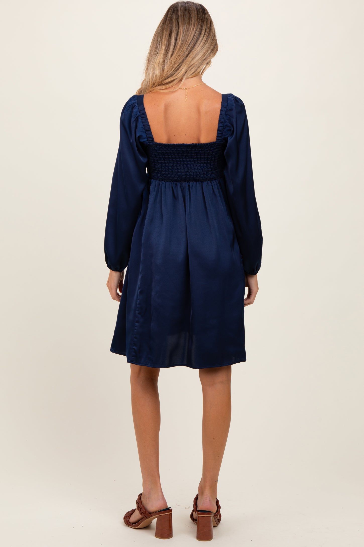 woman wearing a navy blue maternity dress with a smocked bodice and long sleeves, showing the back view