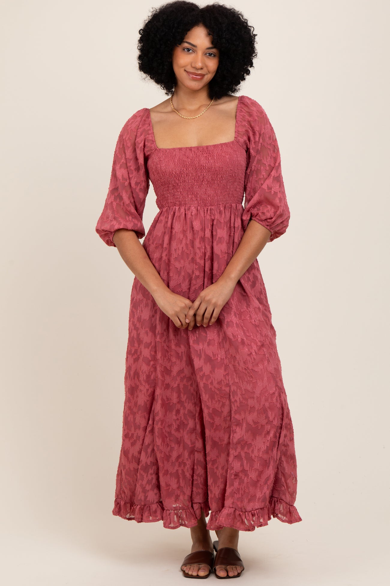 woman wearing a pink floral maxi dress with puff sleeves and a square neckline, standing with hands clasped in front