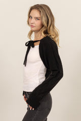 woman wearing a black knit cardigan with a bow tie closure over a white top and styled with dark jeans