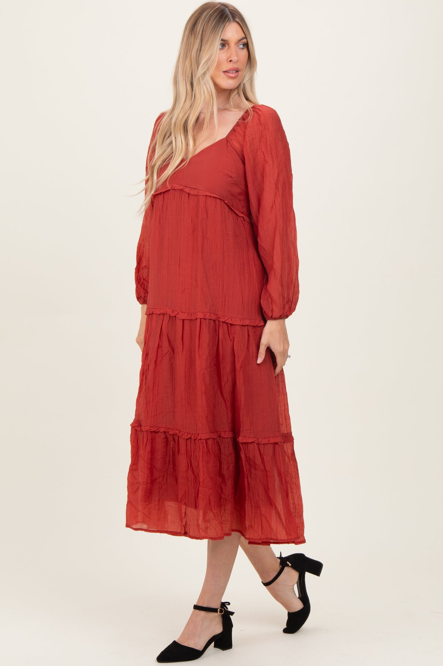 woman wearing a rust red tiered maxi dress with long sleeves and a v-neckline, styled with black heels