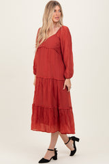 woman wearing a rust red tiered maxi dress with long sleeves and a v-neckline, styled with black heels