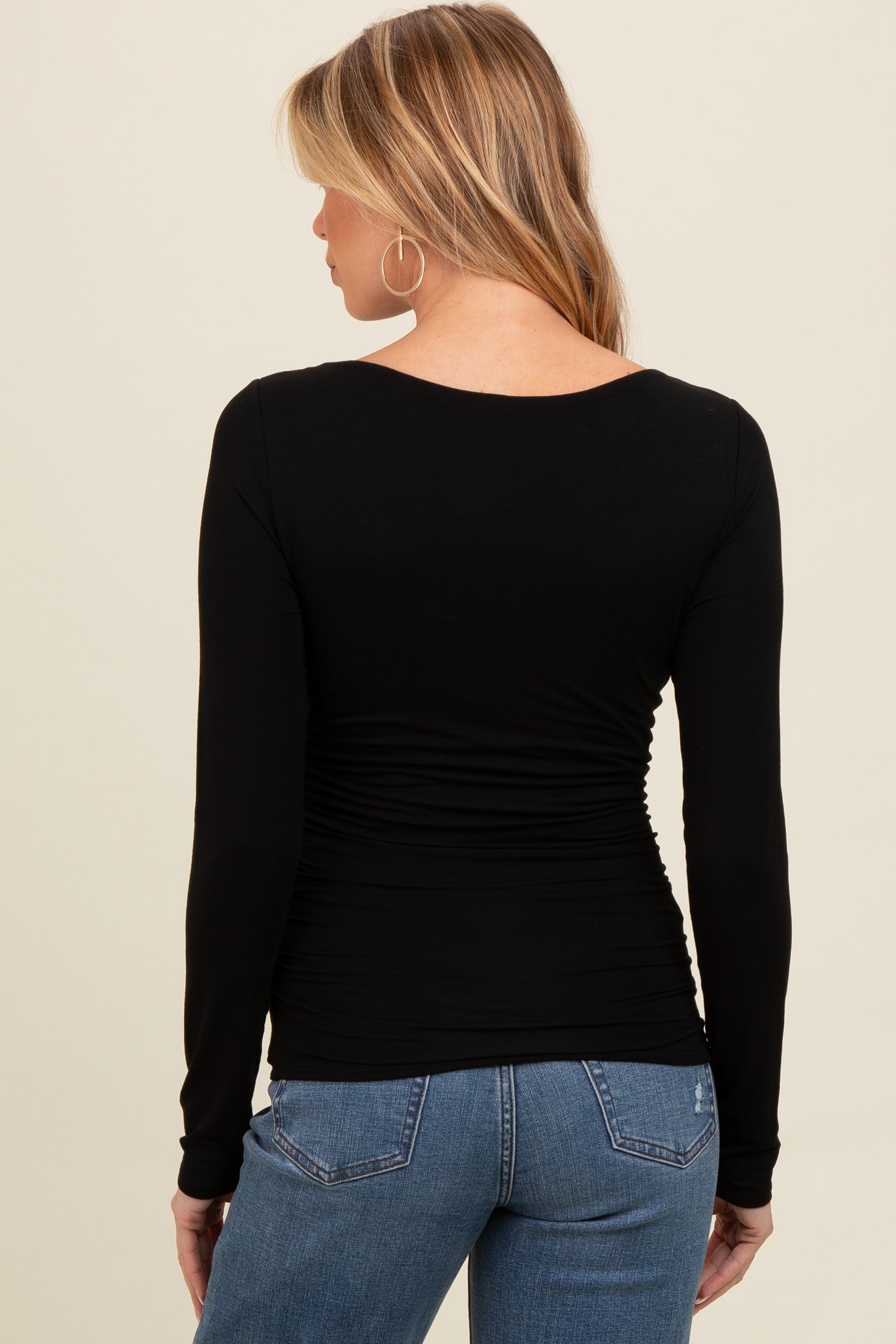 woman wearing a black long sleeve maternity top with gathered details at the waist and blue jeans