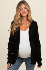 woman wearing a black knitted maternity cardigan over a white tank top and showing her baby bump