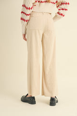 woman wearing beige corduroy wide-leg trousers and a cream sweater with red patterns, viewed from the back