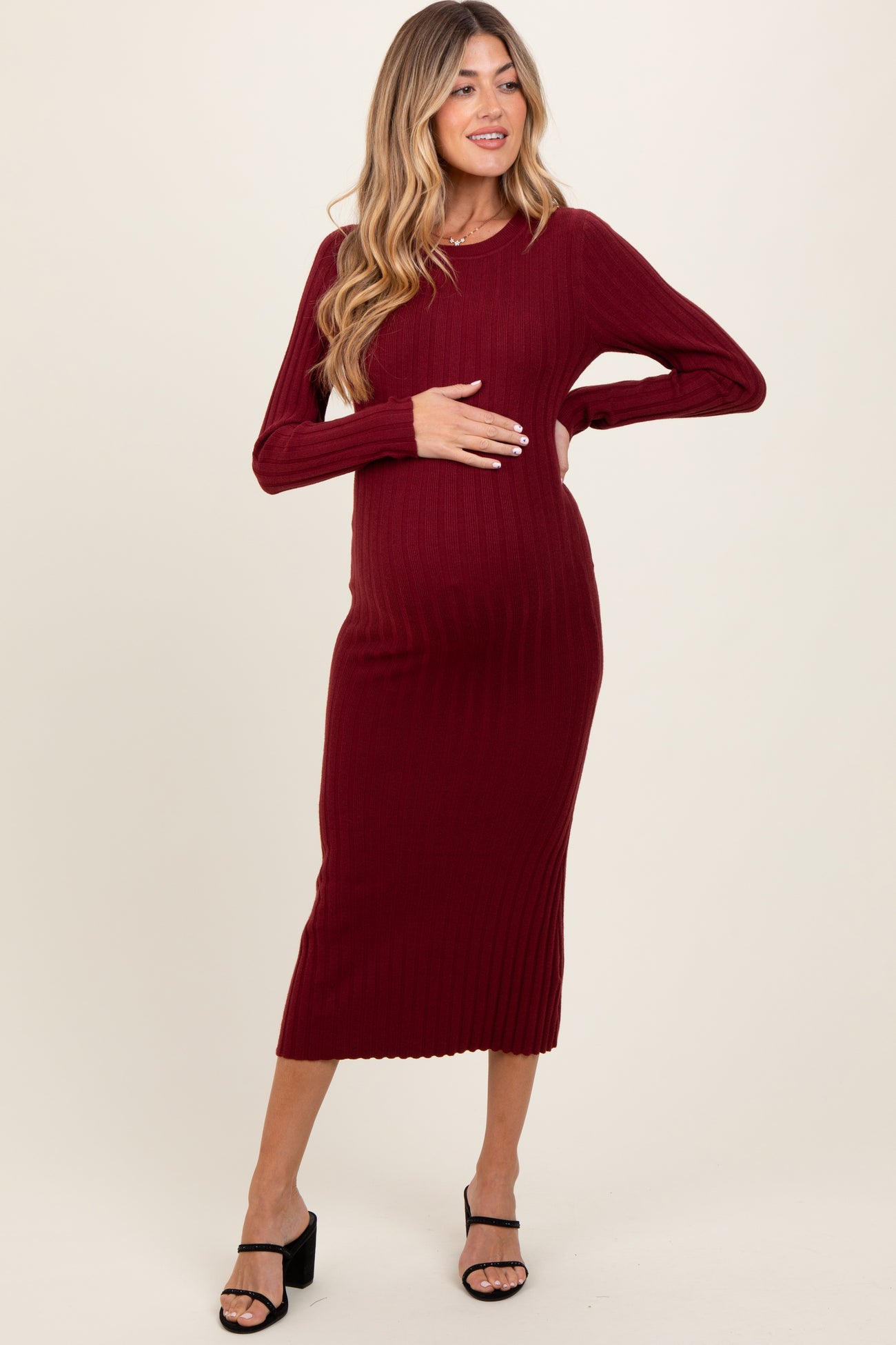 woman wearing a burgundy ribbed knit maternity dress and gently holding her baby bump