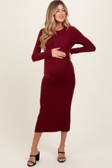 woman wearing a burgundy ribbed knit maternity dress and gently holding her baby bump