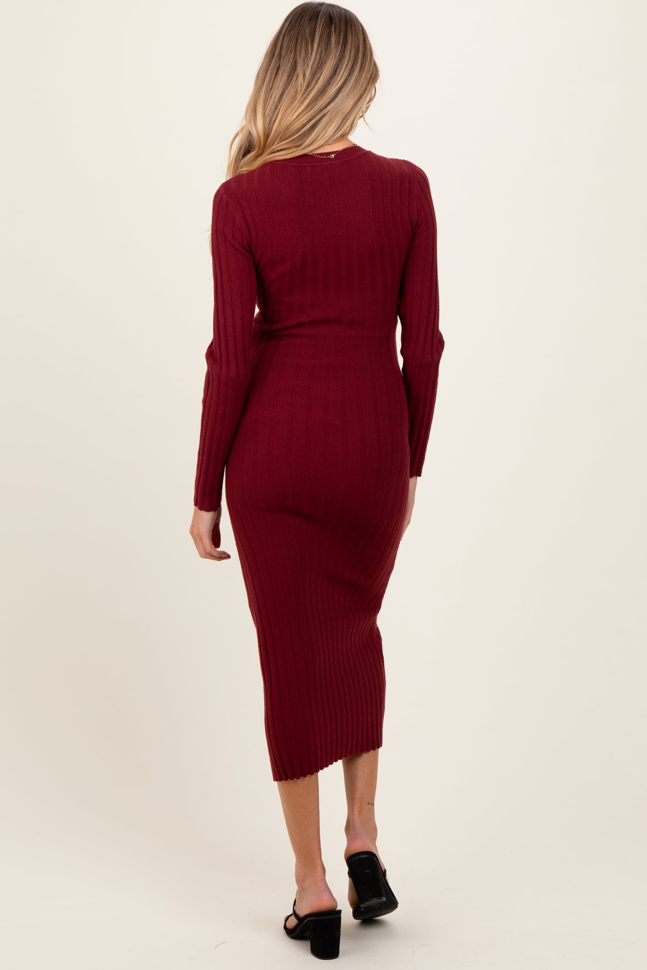 woman wearing a burgundy ribbed maternity dress with long sleeves and a fitted silhouette, showing her baby bump from the back