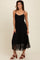 woman wearing a black maxi dress with spaghetti straps and silver embellishments, standing on a neutral background