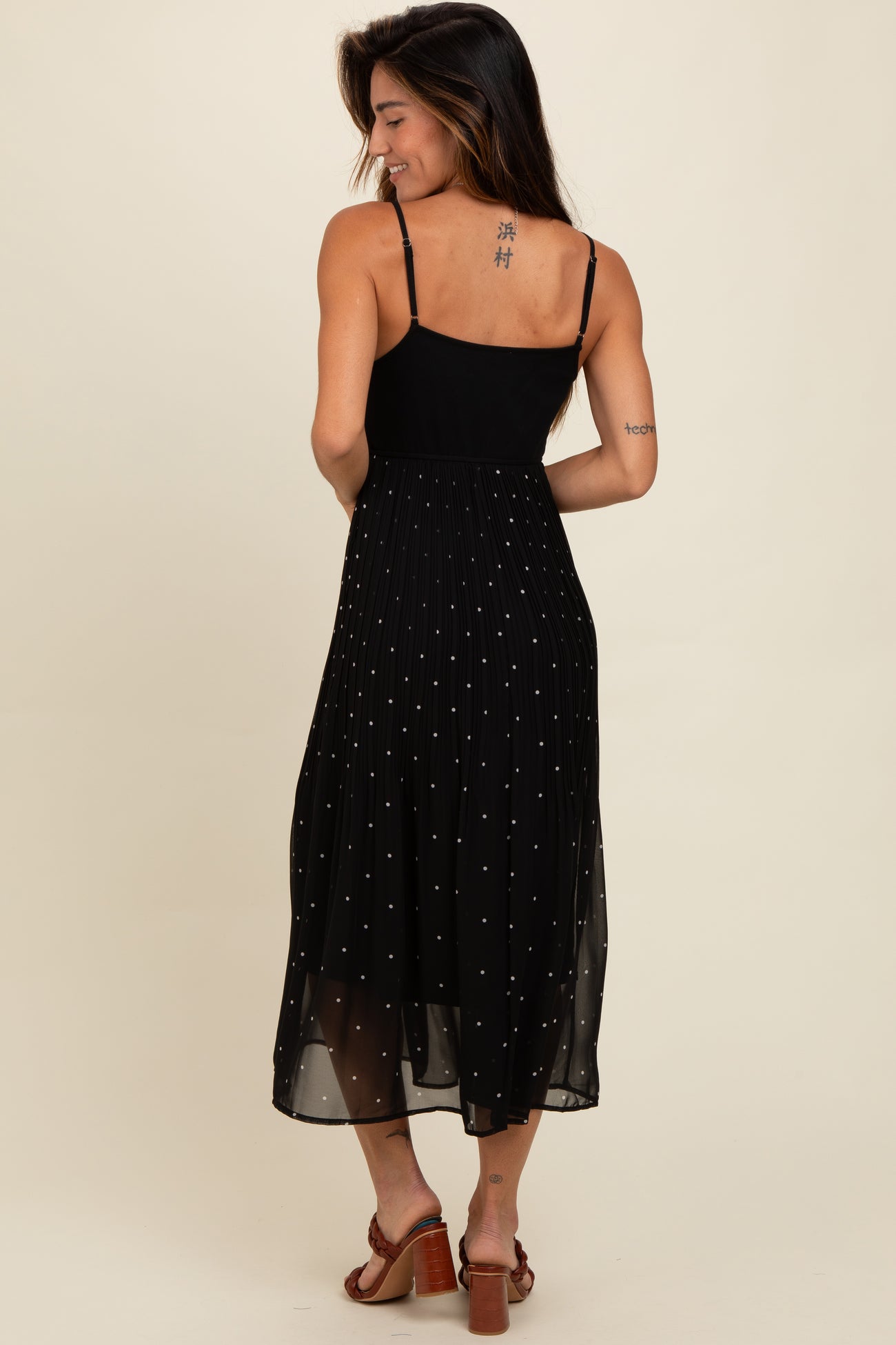 woman wearing a black midi dress with a fitted top and pleated skirt, featuring metallic dot embellishments