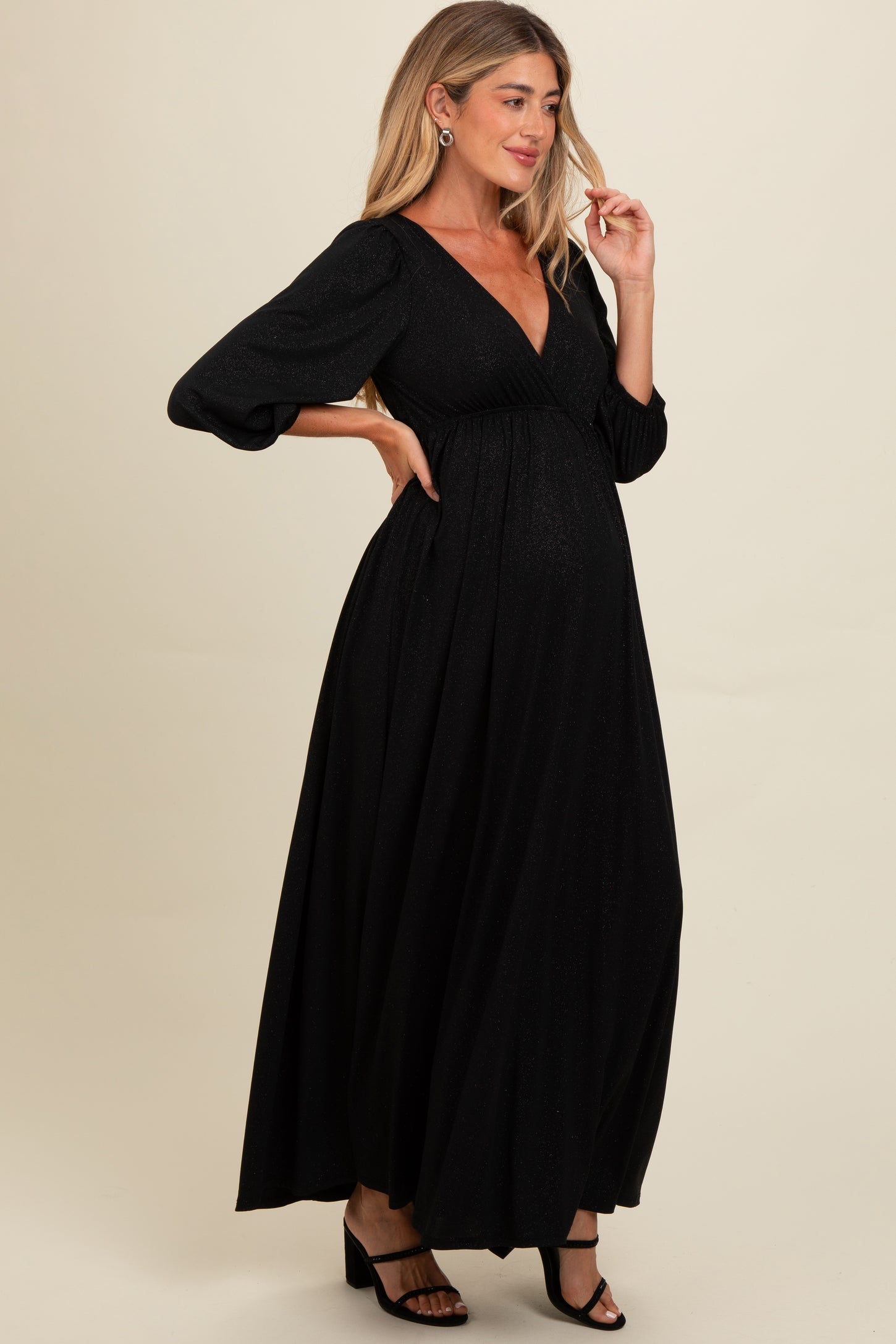 woman wearing a black sparkly maternity maxi dress with long sleeves and a v-neckline, highlighting her baby bump