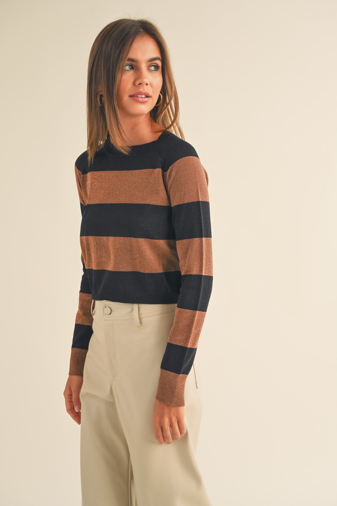 woman wearing a striped brown and black long sleeve sweater with a relaxed fit and high-waisted beige trousers