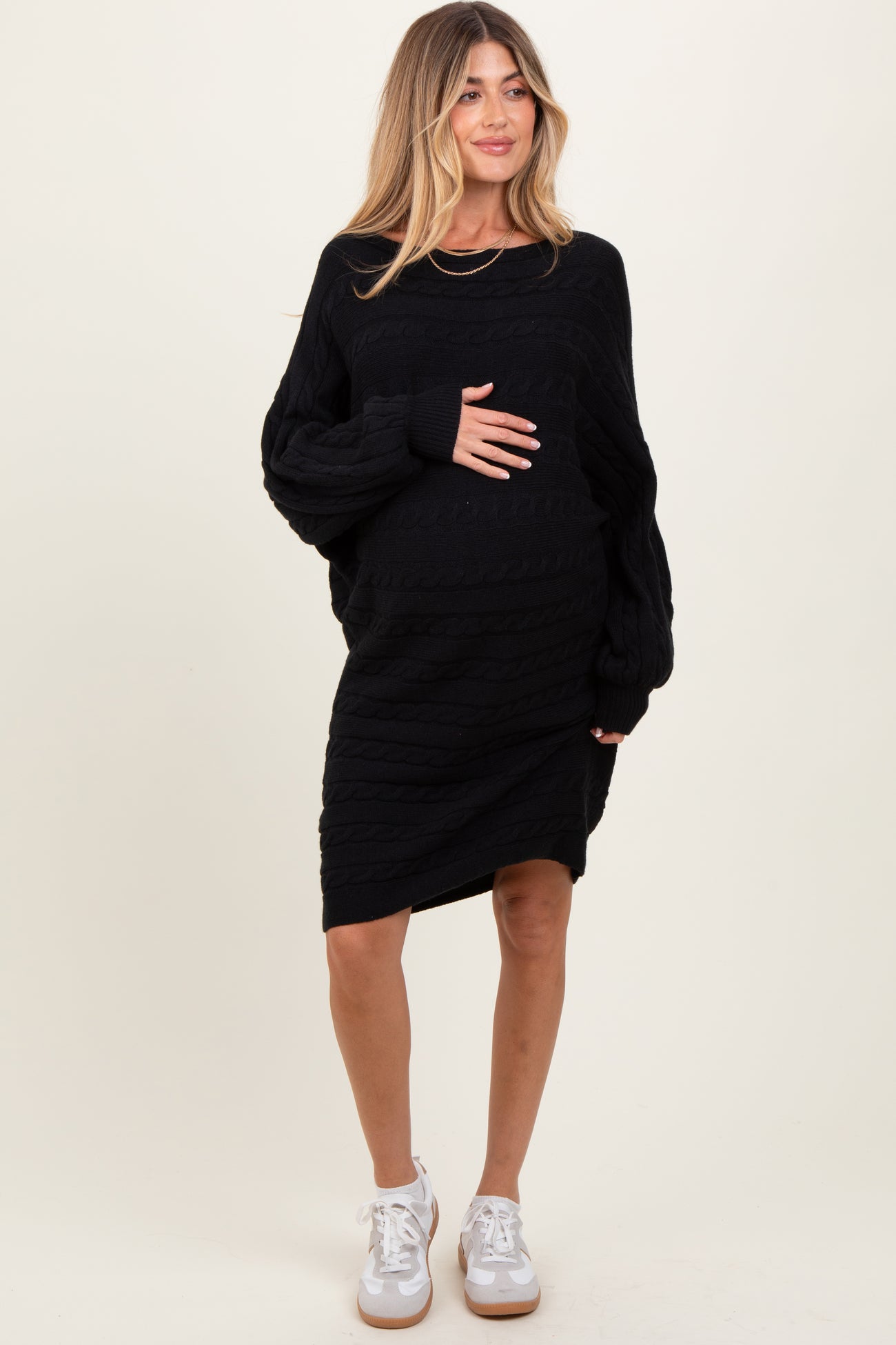 woman wearing a black cable knit maternity dress with long sleeves and holding her baby bump