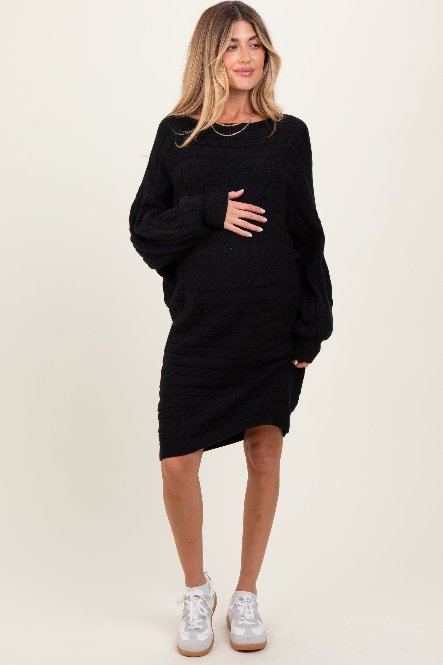 woman wearing a black cable knit maternity dress with long sleeves and holding her baby bump