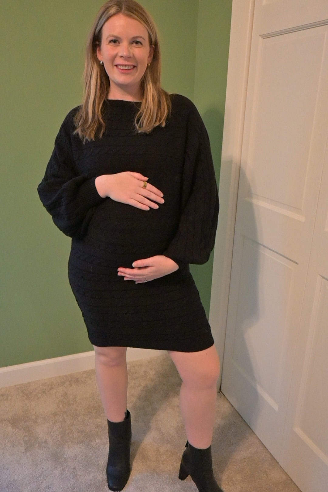 woman wearing a black cable knit short dress and holding her baby bump