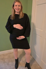 woman wearing a black cable knit short dress and holding her baby bump