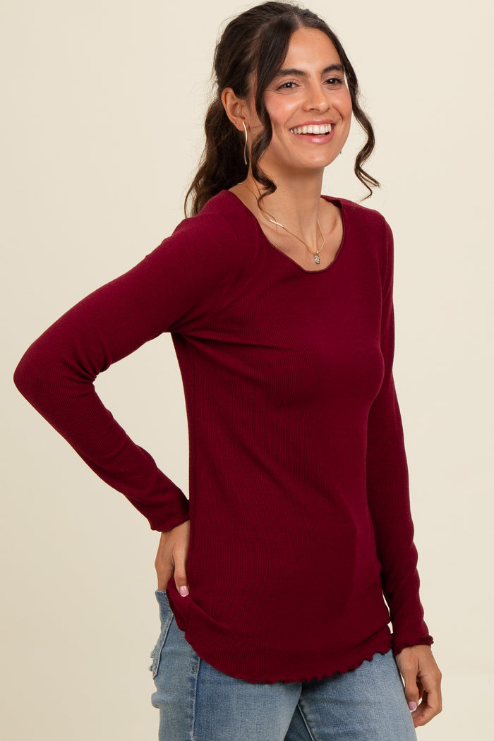 woman wearing a burgundy long sleeve ribbed top with a curved hemline and a relaxed fit