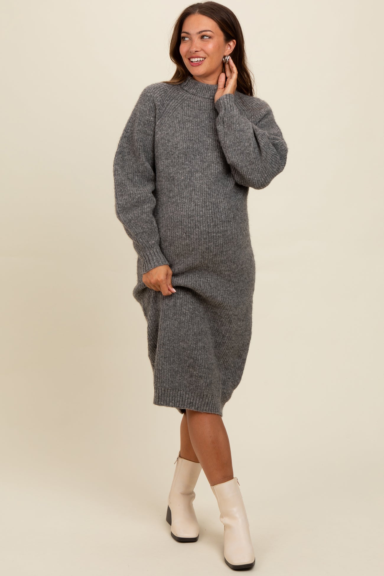 woman wearing a cozy gray ribbed maternity sweater dress, gently cradling her baby bump