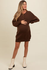 woman wearing a brown maternity sweater dress with buttons and a visible baby bump, styled with white ankle boots
