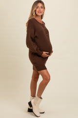 woman wearing a brown maternity sweater dress with buttons and holding her baby bump
