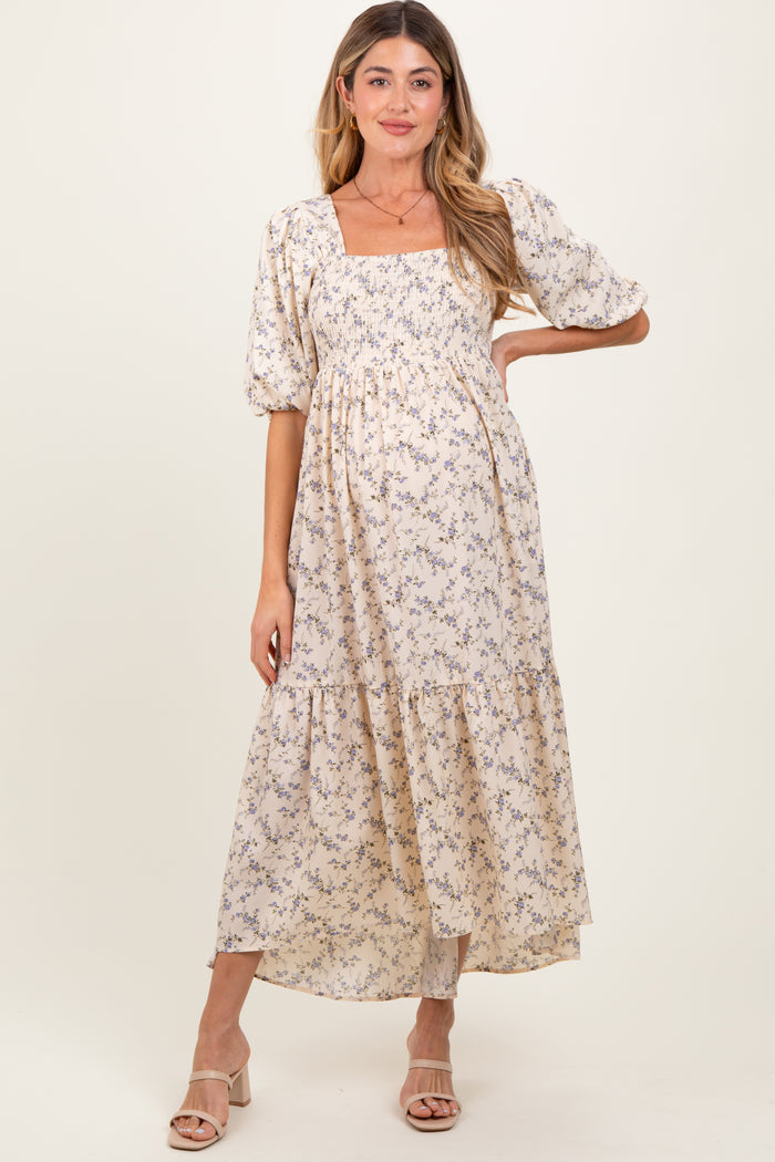 woman wearing a light beige floral maternity dress with puff sleeves and tiered skirt, showcasing her baby bump