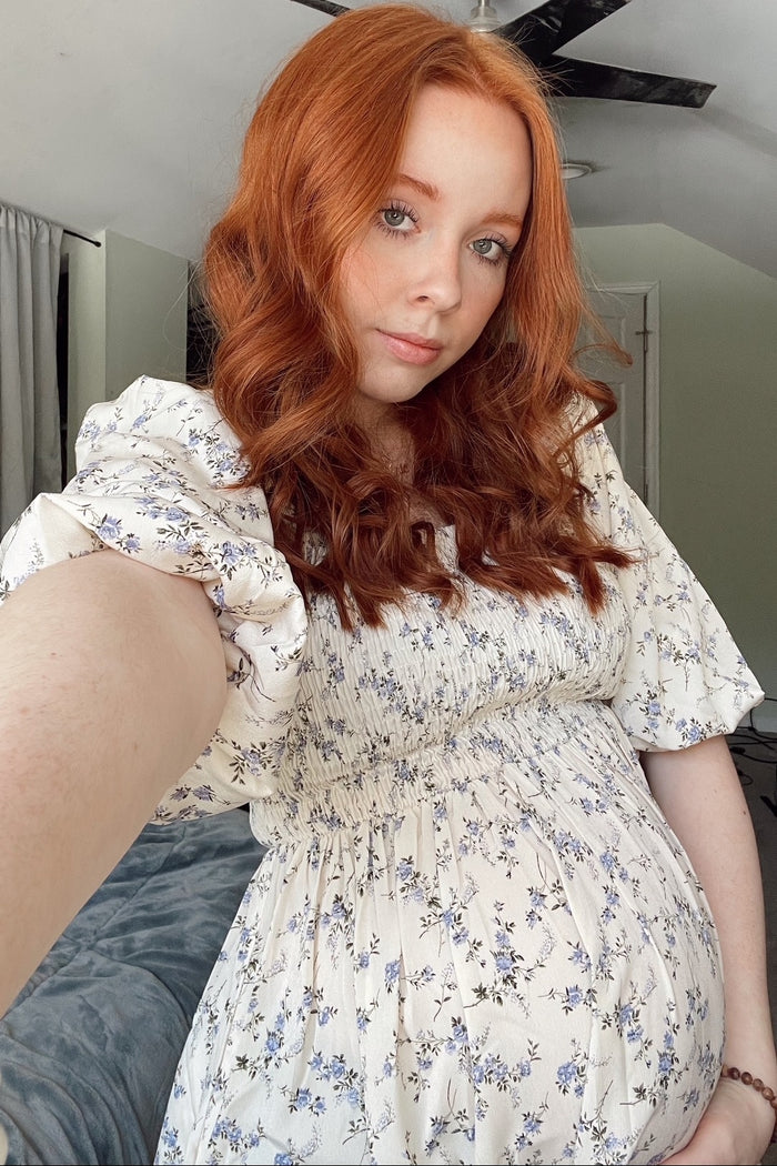 woman wearing a floral print maternity dress with puff sleeves and holding her baby bump
