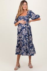 woman wearing a navy blue floral print maternity dress with puff sleeves and a ruffled hem, holding her baby bump