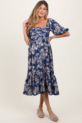 woman wearing a navy blue floral print maternity dress with a square neckline and tiered hem, showcasing her baby bump