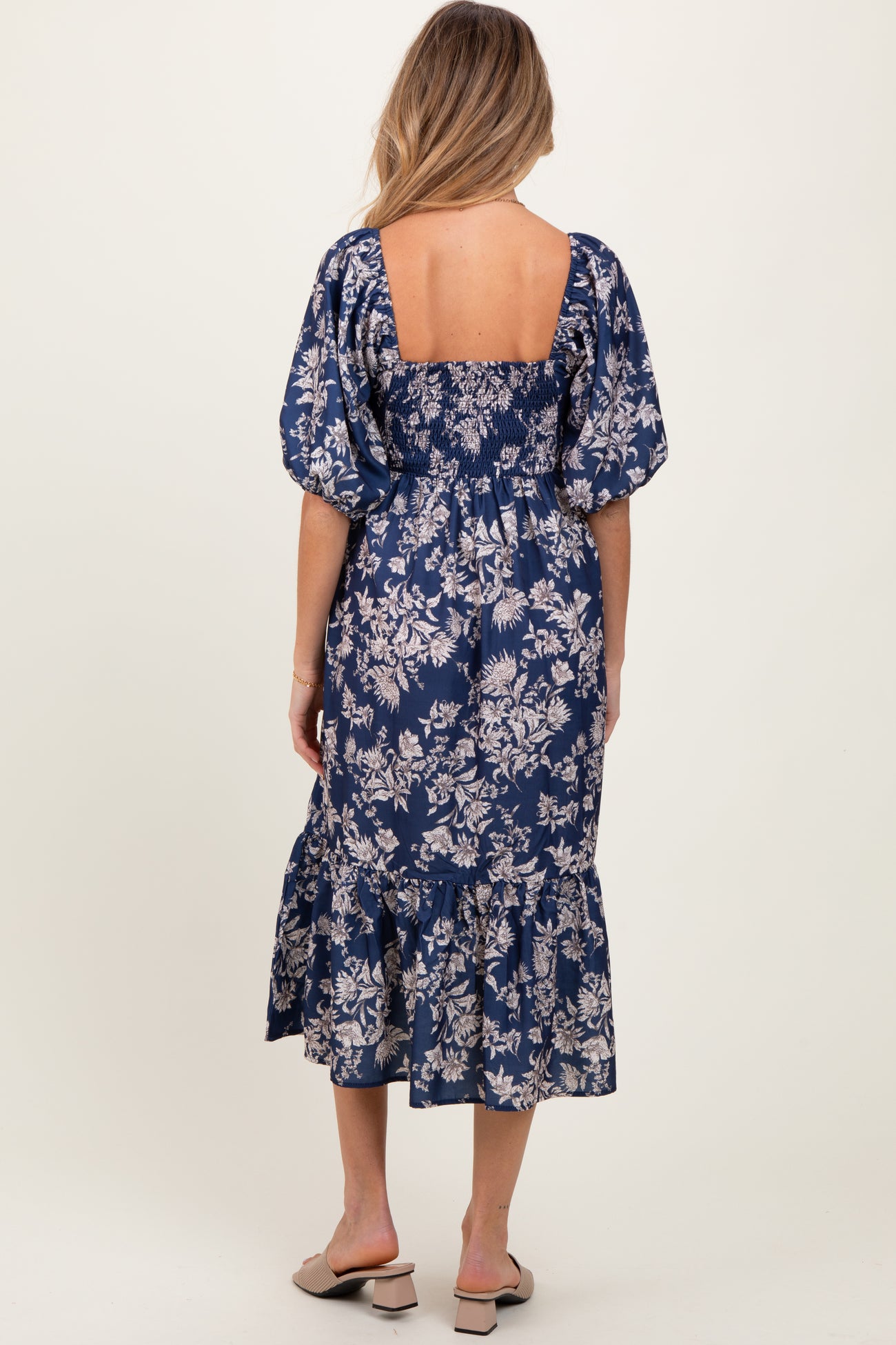 woman wearing a navy blue floral print maternity dress with puff sleeves and a ruffled hem, showing her baby bump