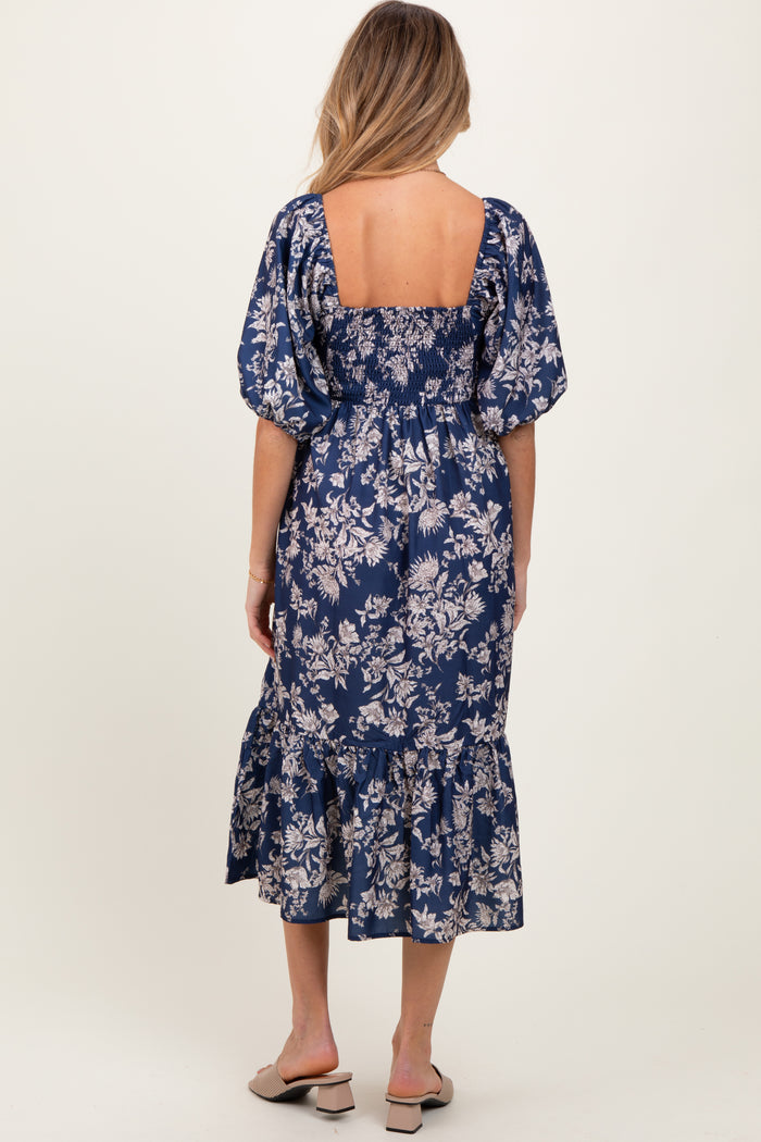 woman wearing a navy blue floral print maternity dress with puff sleeves and a ruffled hem, showing her baby bump