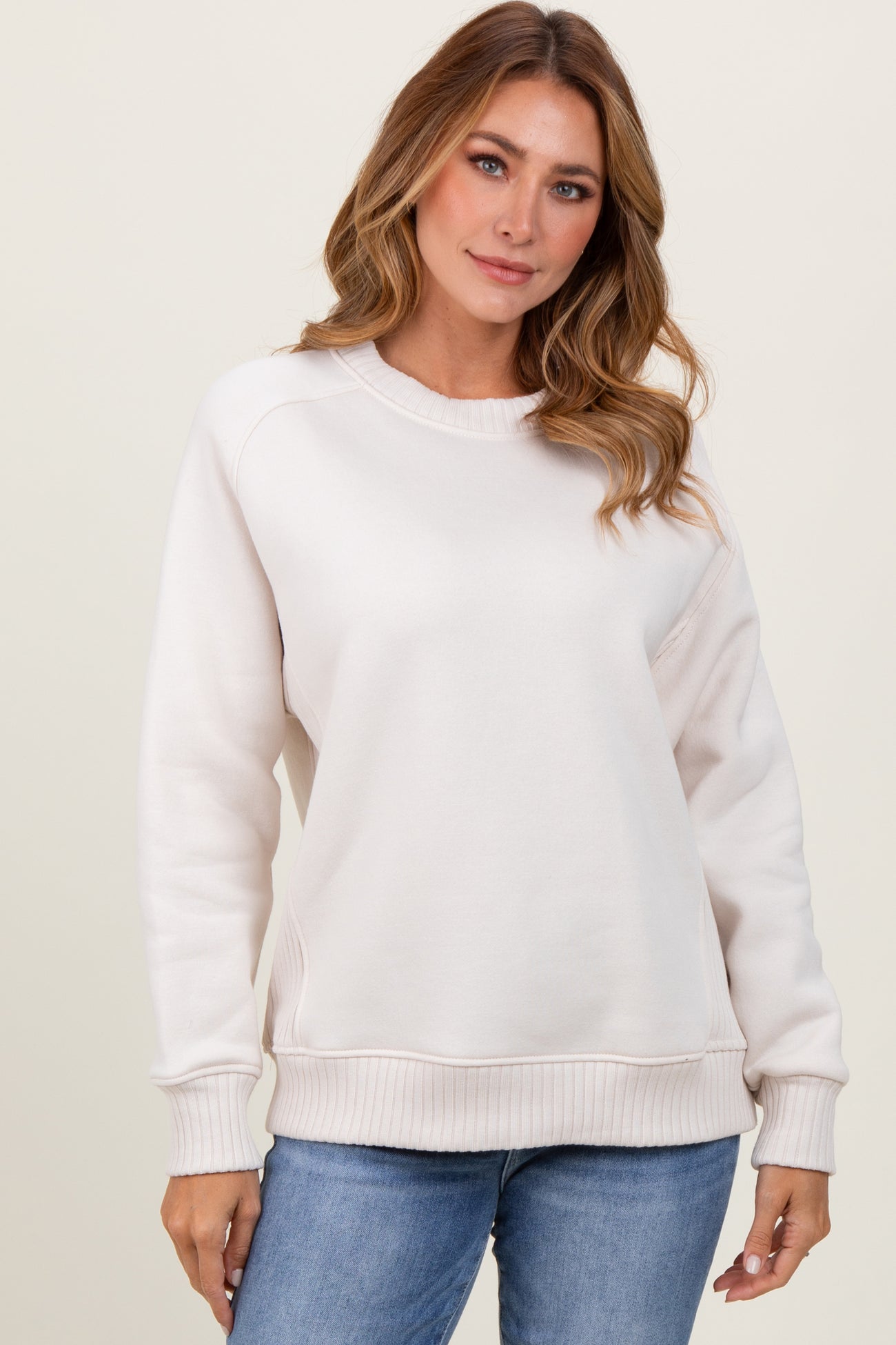woman wearing a light beige long sleeve sweatshirt with ribbed cuffs and hem, paired with blue jeans