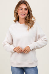 woman wearing a light beige long sleeve sweatshirt with ribbed hem and cuffs, smiling at the camera