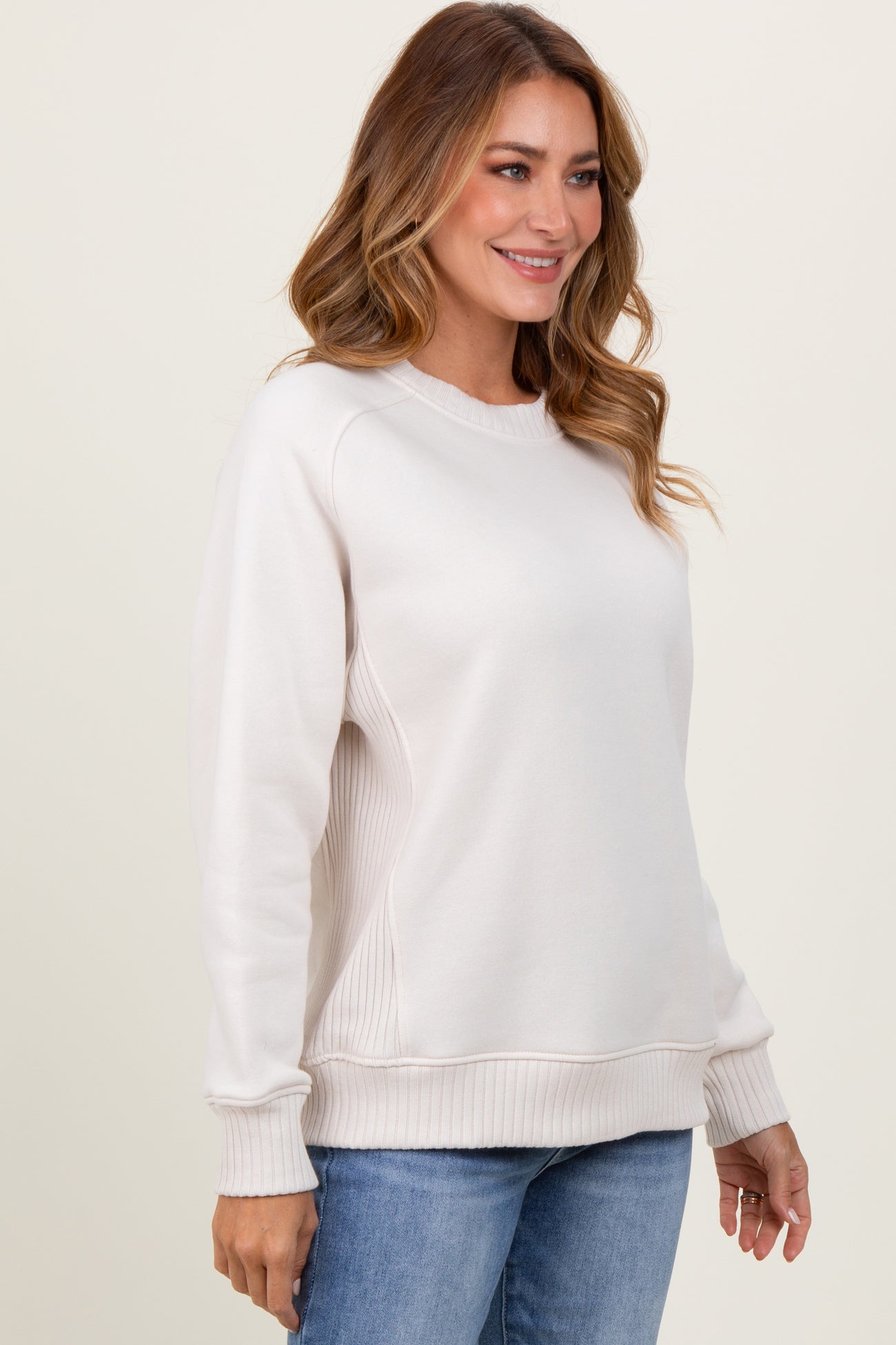 woman wearing a light beige long sleeve sweatshirt with ribbed details and a relaxed fit